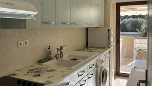 Cozinha compacta com máquina de lavar embutida, uma pia pequena e janela com vista para o verde lá fora.