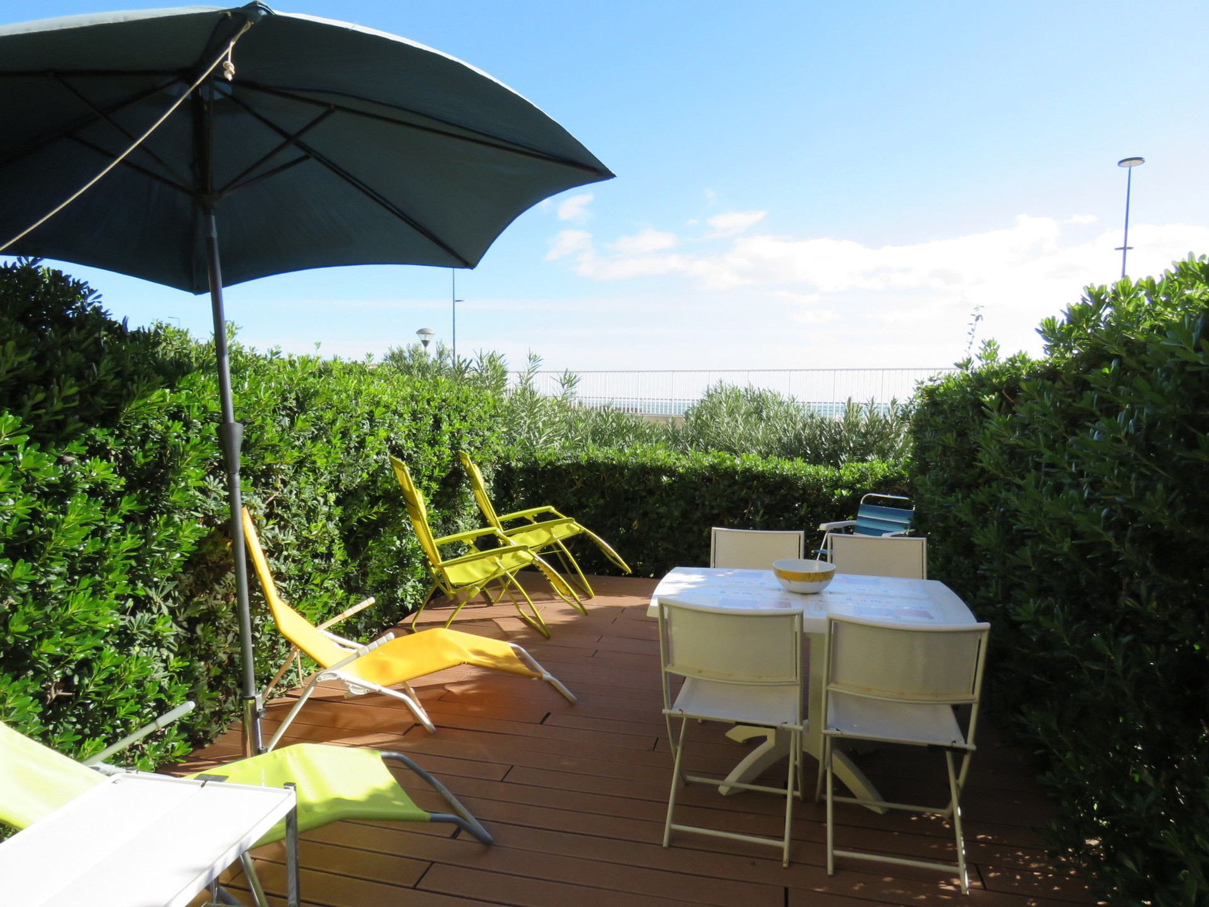 An outdoor patio with a table and chairs, a large umbrella, and a view of the sea.