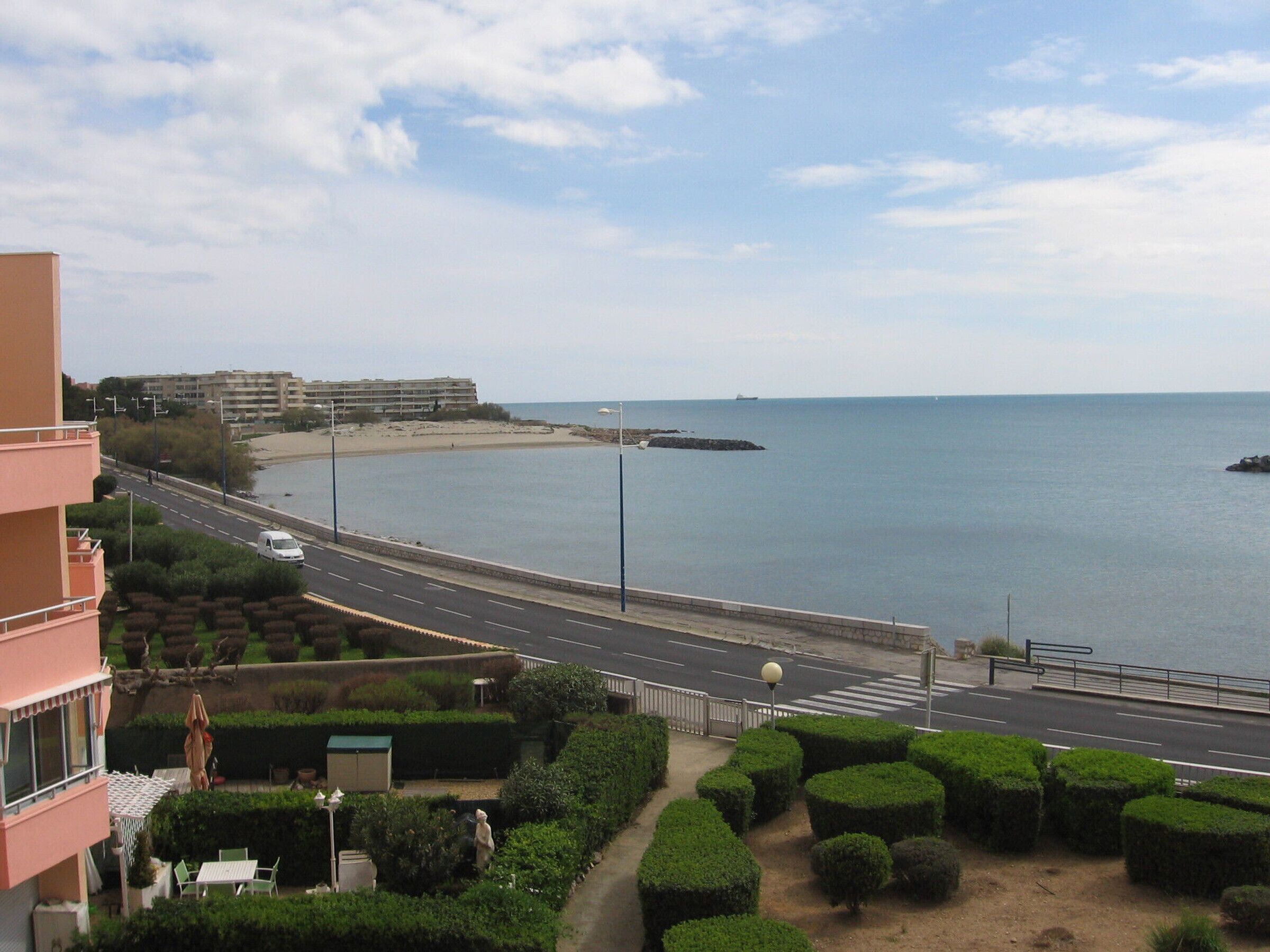 Eine Küstenstraße mit Blick auf das Meer, ein Fußweg und ein Gebäude mit Balkonen.