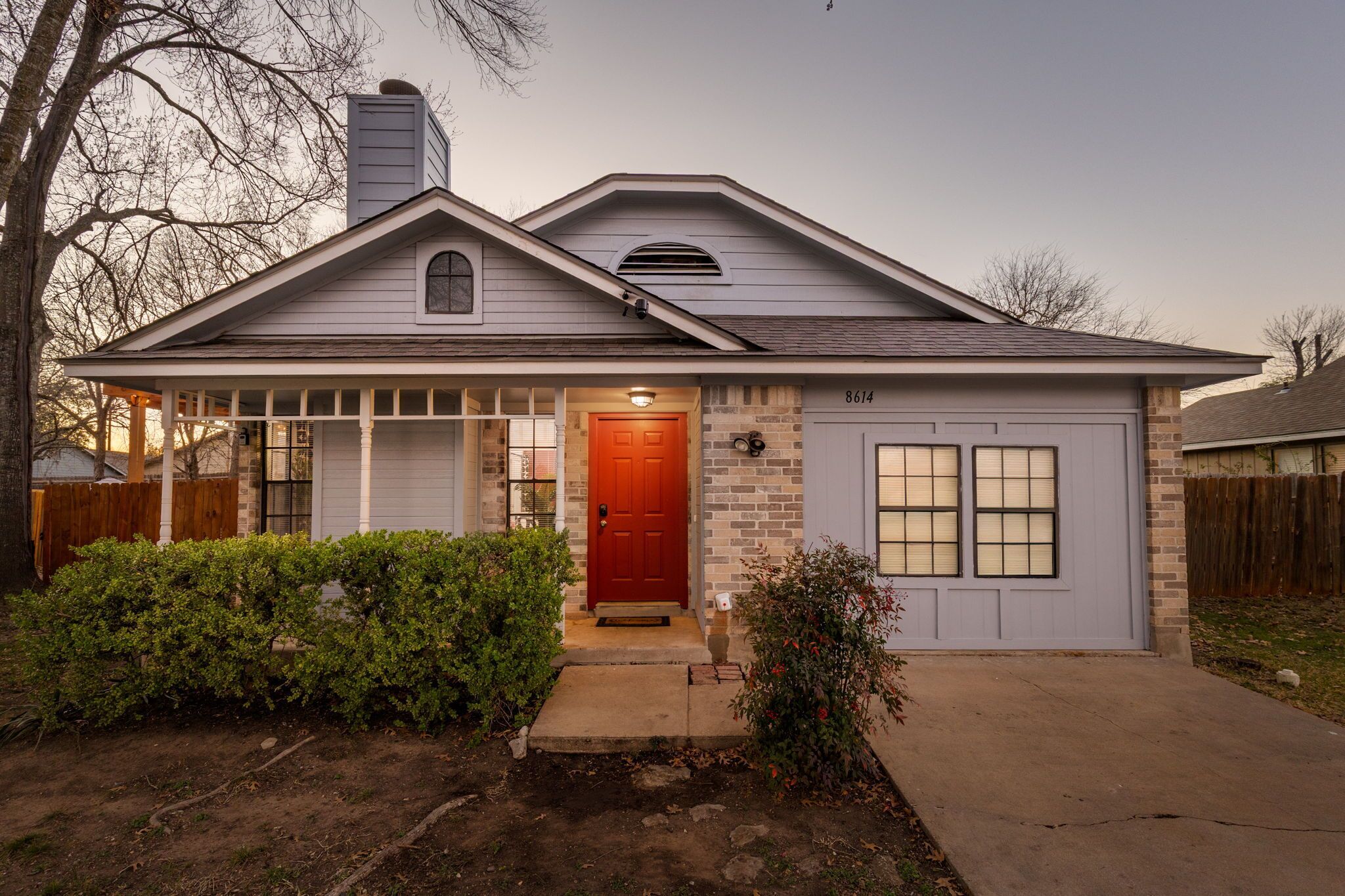 A single-story house with a red front door, a garage, and a brick exterior.