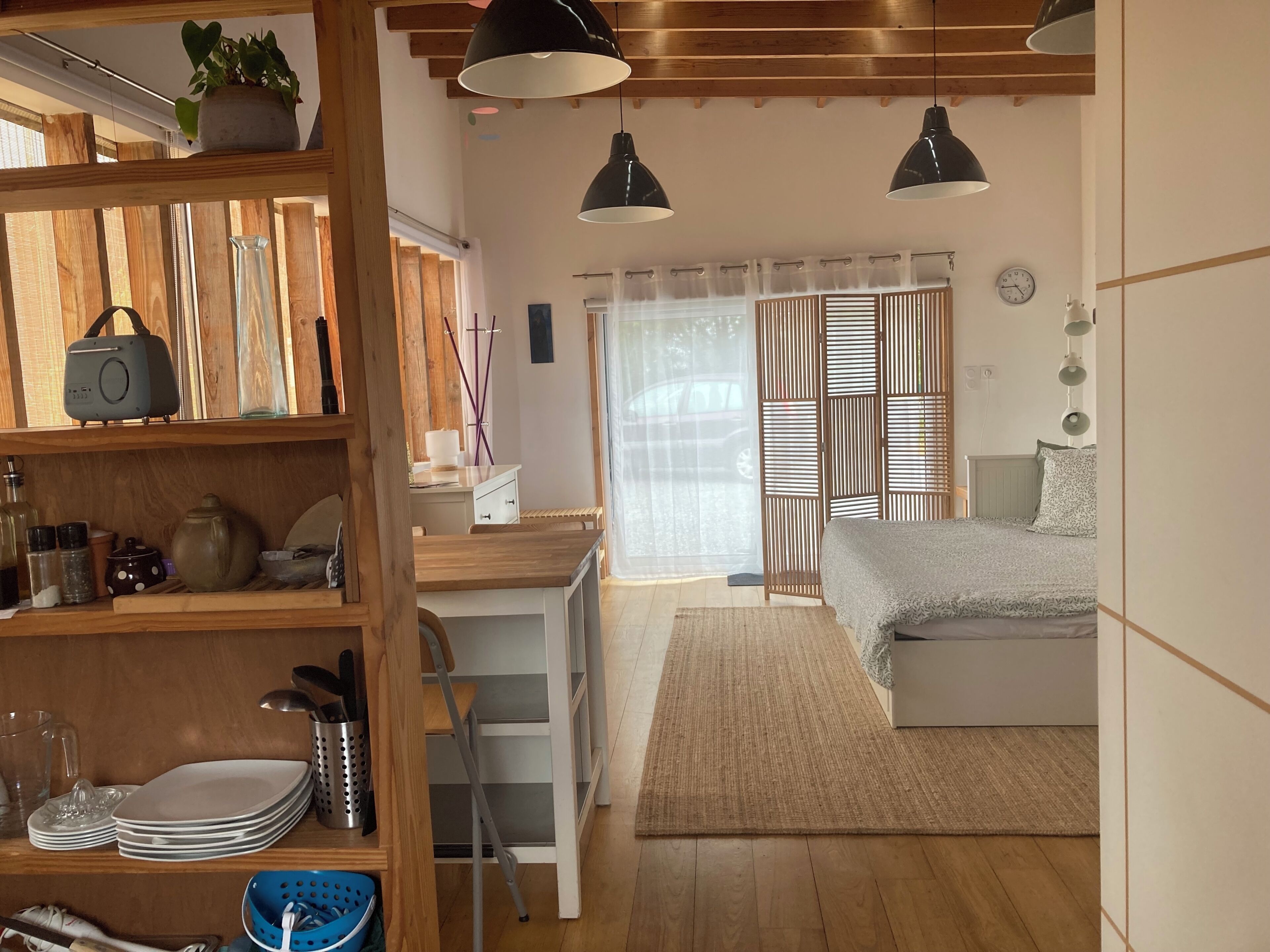 Una habitación con una cama, un escritorio y una estantería con utensilios de cocina.