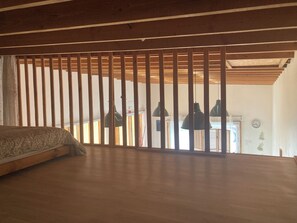 A room with a bed, wooden slats, hanging pendant lights, and a visible door leading to another room. - L'atelier, 800 meters from the sea, unique lodging in an old neighborhood (Plouescat)