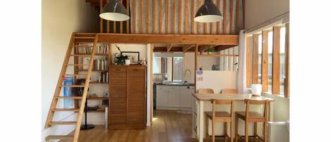 Ein Loft-Zimmer mit einer Holztreppe, einem Essbereich und einer Küche.