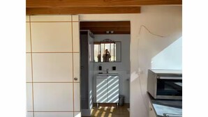Una habitación con techo de madera, pared de azulejos, espejo, lavamanos y microondas.