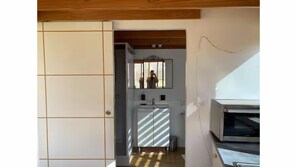 Une pièce avec un plafond en bois, un mur recouvert de carreaux, un miroir, un lavabo et un four à micro-ondes.