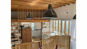 Ein geräumiger Raum mit hoher Decke, Holzbalken, einem Essbereich mit Tisch und Stühlen sowie einer Küchenzeile mit Spüle und Schränken.