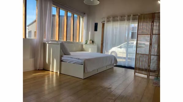 Ein Schlafzimmer mit Bett, Heizkörper, Fenster und Blick auf ein Auto draußen.