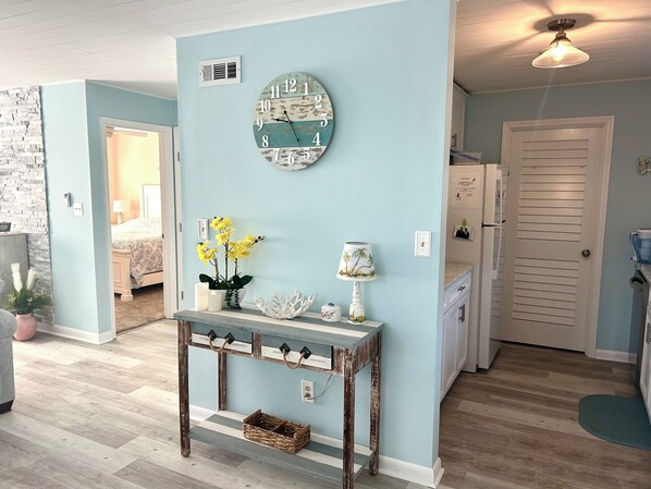 A room with a light blue wall, a wooden console table with a clock, a lamp, and a potted plant.