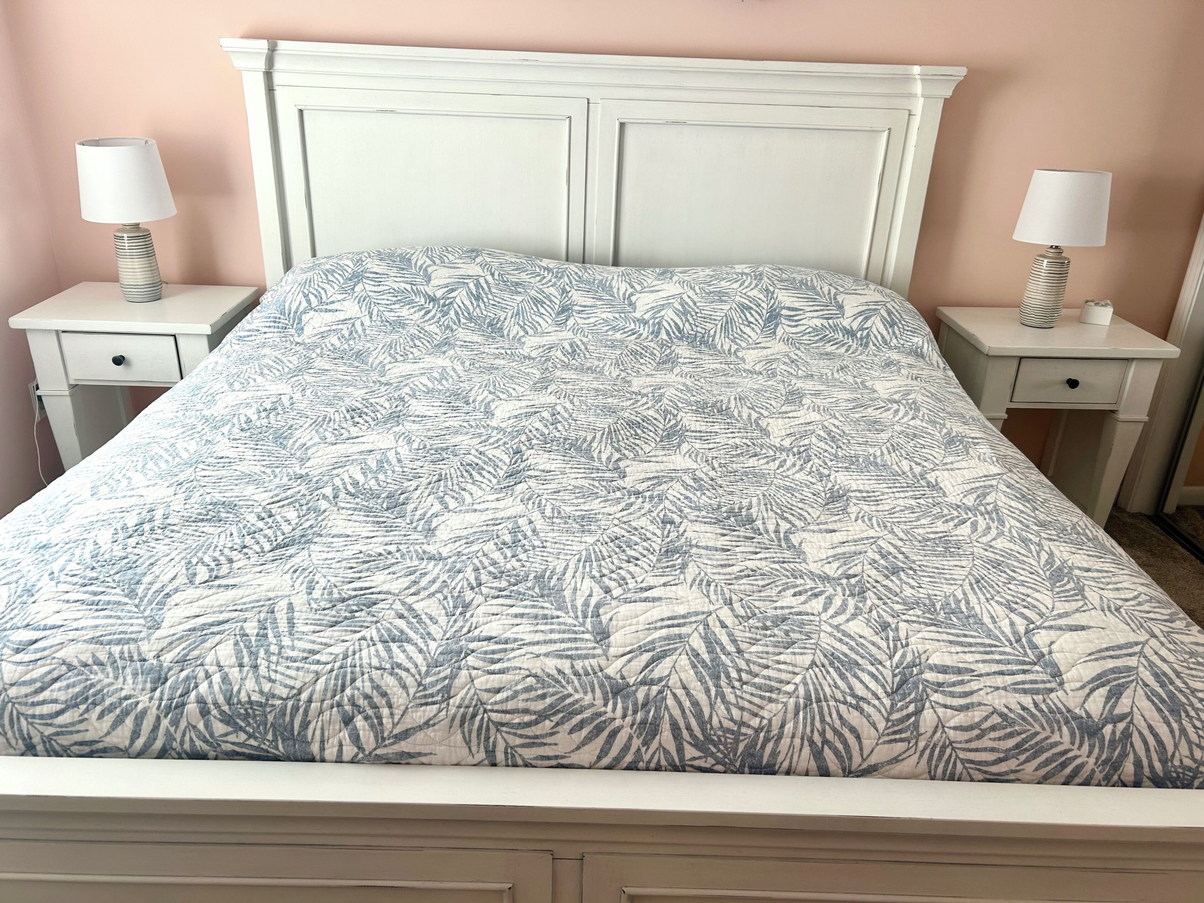 A bed with a leaf-patterned bedspread, two bedside tables with lamps, and a white headboard.
