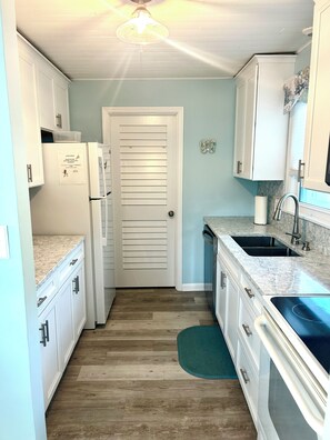 A narrow kitchen with white cabinets, a refrigerator, a sink, and a ceiling fan.
