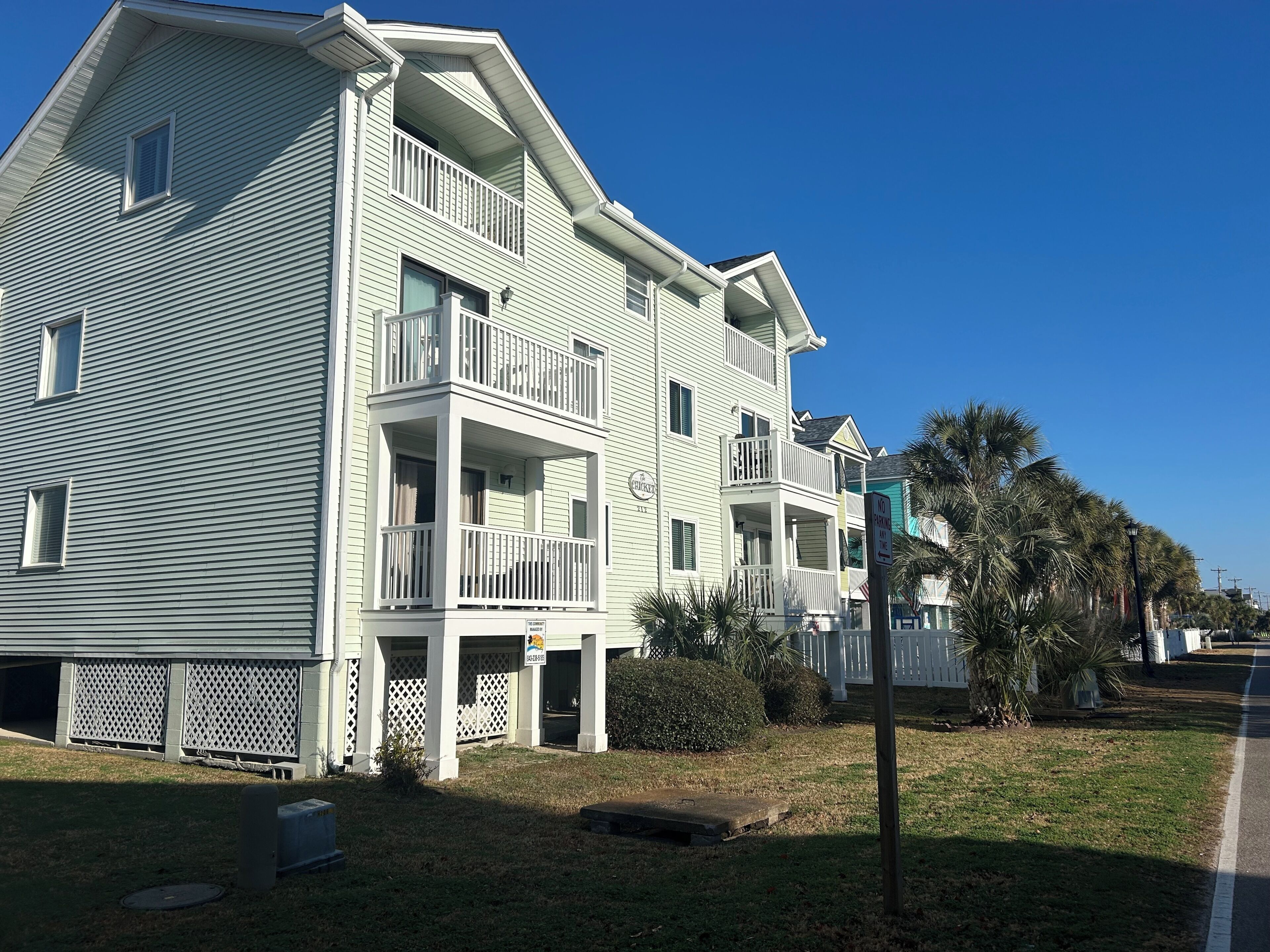 A two-story building with balconies, a gated entrance, and a clear sky.