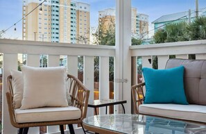 Ein Balkon mit Korbmöbeln, einem Glastisch und Blick auf hohe Gebäude.