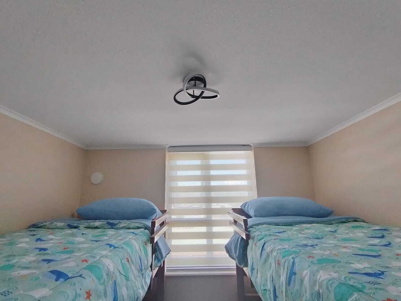 A room with two beds, a ceiling fan, and a window with blinds.