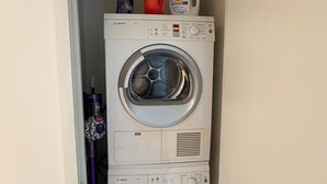 A compact laundry room with two stacked washing machines, a bottle of Tide detergent, and a red mug. - Cozy 1-bedroom apartment in delightful Downtown Los Angeles with AC and gym (Los Angeles)