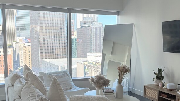 A modern living room with a large sofa, a coffee table, and a TV mounted on the wall. - Cozy 1-bedroom apartment in delightful Downtown Los Angeles with AC and gym (Los Angeles)