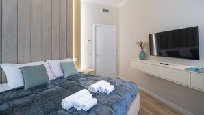 Et moderne hotelværelse med seng, fladskærms-tv, et hvidt konsolbord og en dør.