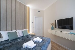 Ein modernes Hotelzimmer mit Bett, Flachbildfernseher, weißem Konsolentisch und einer Tür.