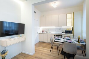 Eine moderne Küche mit Flachbildfernseher, Holzschränken und einem Essbereich mit Tisch und Stühlen für zwei Personen.