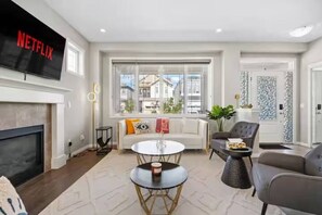 A living room with a fireplace, a TV mounted on the wall, a sofa, a coffee table, and a dining area with chairs. - Spacious 5-bedroom house in tranquil Calgary perfect for families (Calgary)