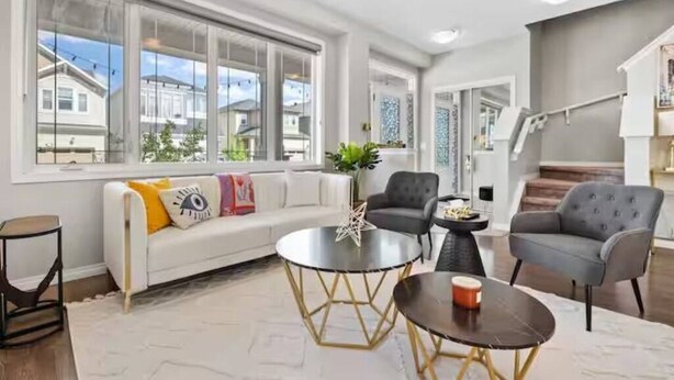 Una sala de estar moderna con un sofá blanco, dos sillones, una mesa de centro y una escalera al fondo.
