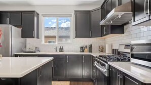 Una cocina moderna con armarios oscuros, una estufa de acero inoxidable y un ventanal con vistas al exterior.