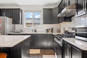 A modern kitchen with dark cabinets, a stainless steel range, and a window with a view of the outside. - Spacious 5-bedroom house in tranquil Calgary perfect for families (Calgary)