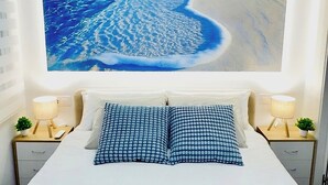 Een slaapkamer met een groot bed, twee nachtkastjes en een aan de muur hangend schilderij van een strandgezicht.