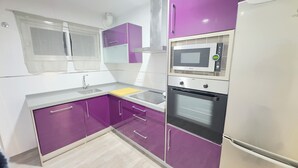 Een compacte keuken met een spoelbak, magnetron, oven en paarse kastjes.