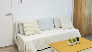 Een moderne woonkamer met een bank, een bijzettafeltje met planten, een schilderij aan de muur en een houten garderobe.