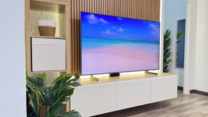 Een flatscreen-tv op een witte tv-meubel met een strandbeeld op het scherm.