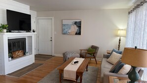 Una sala de estar con chimenea, televisor, cuadro, sofá, mesa de centro y lámpara.