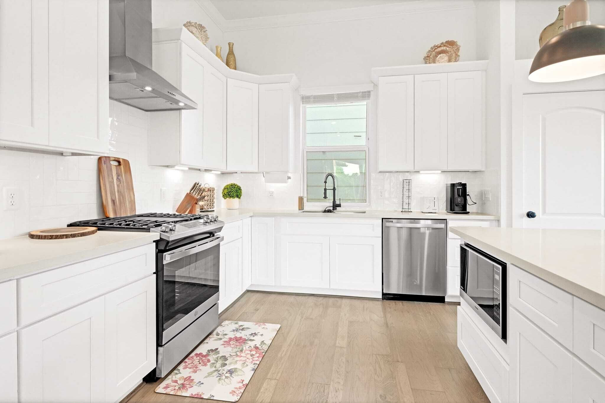 A modern kitchen with white cabinetry, stainless steel appliances, and a wooden floor.