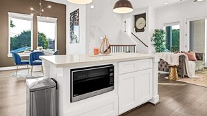 Une cuisine moderne dotée d’un four à micro-ondes encastré, de meubles blancs, d’un éclairage suspendu et offrant une vue sur l’extérieur.