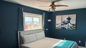 A bedroom with a bed, a ceiling fan, a window with curtains, a wall-mounted lamp, and a painting. - Downtown Gulf Shores Beach -Best Spot in Complex W/Panoramic Views-Pet Friendly (Gulf Shores)