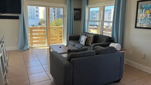 A living room with a sofa, a coffee table, and a TV mounted on the wall. - Downtown Gulf Shores Beach -Best Spot in Complex W/Panoramic Views-Pet Friendly (Gulf Shores)