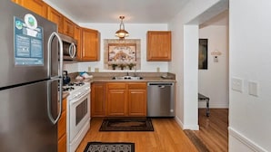 A kitchen with wooden cabinets, stainless steel appliances, a stone backsplash, and a hanging light fixture. - Mountain Bearadise (Big Bear Lake)
