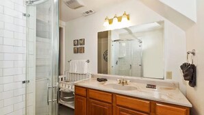 A bathroom with a glass shower enclosure, a double sink vanity, and a large mirror with a light fixture above. - Mountain Bearadise (Big Bear Lake)