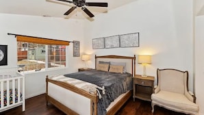 A bedroom with a bed, a chair, a nightstand, a window, and a ceiling fan. - Mountain Bearadise (Big Bear Lake)
