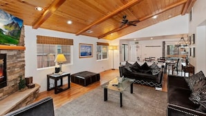 A spacious living area with a stone fireplace, wooden ceiling beams, and a modern black sofa set. - Mountain Bearadise (Big Bear Lake)