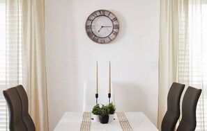 Ein Esstisch mit zwei Stühlen, einer Wanduhr und zwei Kerzen, außerdem ein Blumentopf auf dem Tisch.