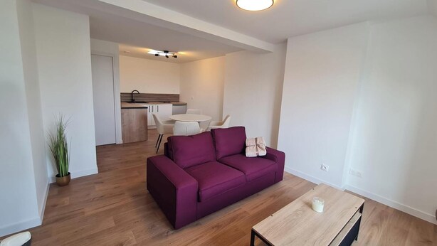 A modern living room with a purple sofa, a wooden coffee table, and a kitchen in the background. - Ideal for professionals on assignment (Festubert)