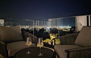 A balcony with two chairs and a table, two glasses of wine, and a city view at night. - Stunning home in Seget Donji (Seget Donji)