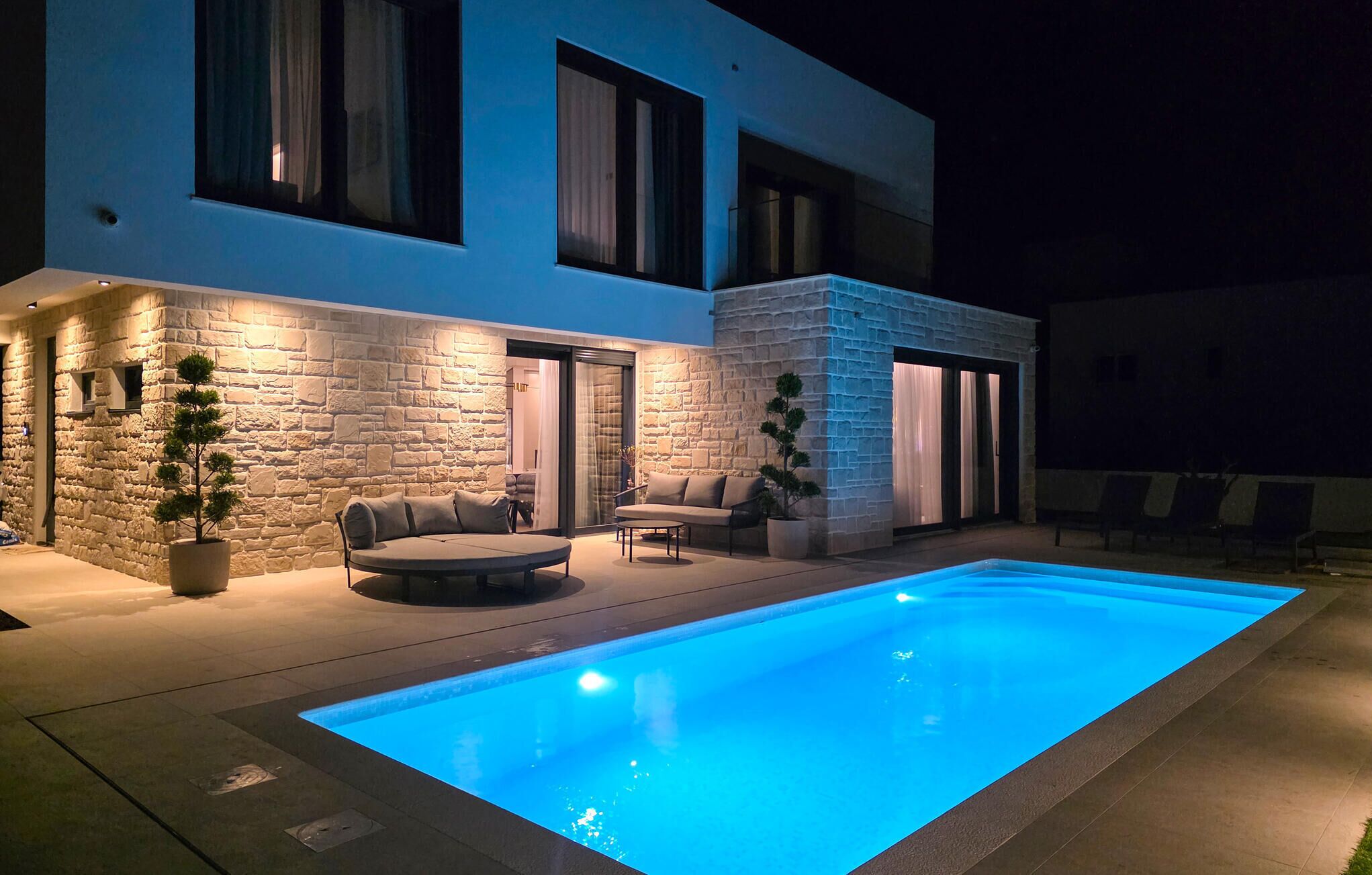 A modern house with a swimming pool, stone walls, and a patio with outdoor furniture.