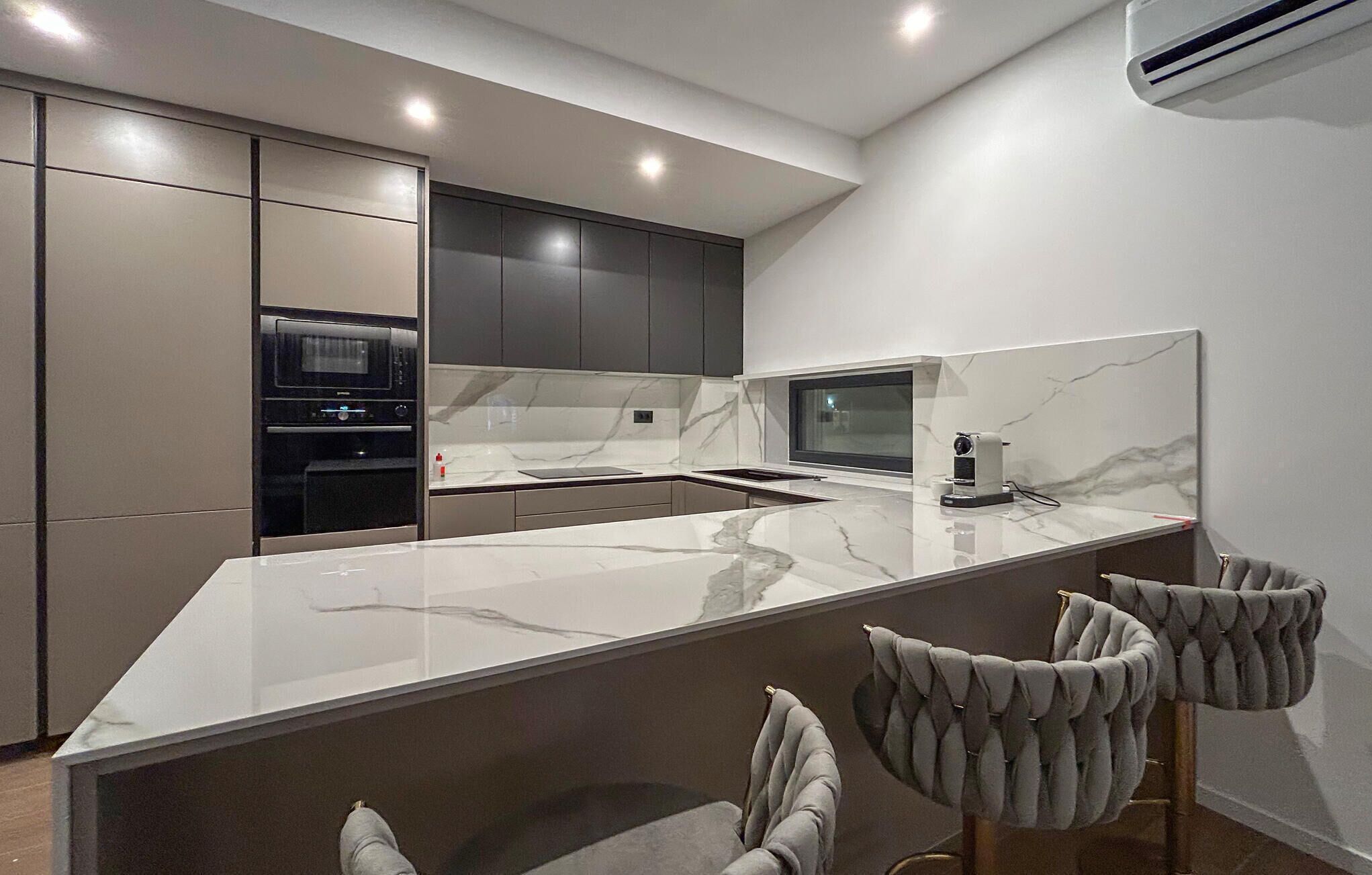 A modern kitchen with a marble countertop, built-in appliances, and a bar area with seating.