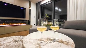 Ein modernes Wohnzimmer mit Kamin, Flachbildfernseher und zwei Weingläsern auf einem Marmortisch.