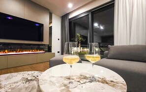 Ein modernes Wohnzimmer mit Kamin, Flachbildfernseher und zwei Weingläsern auf einem Marmortisch.