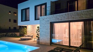 Ein modernes Haus mit Schwimmbad, Steinmauer und Glastür, die auf eine Terrasse führt.