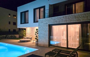 Ein modernes Haus mit Schwimmbad, Steinmauer und Glastür, die auf eine Terrasse führt.