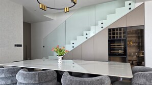 Ein moderner Essbereich mit einem Tisch mit Glasplatte, grauen Polstermöbelstühlen, einer Treppe mit Glastrennwand und einer dekorativen Vase mit Blumen.