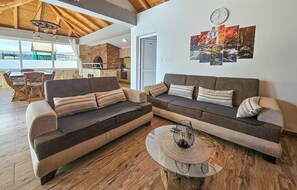Een woonkamer met een hoekbank, een ronde glazen salontafel en een open haard.